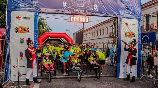 Pelotão de corredores em prova de rua com público ao redor.